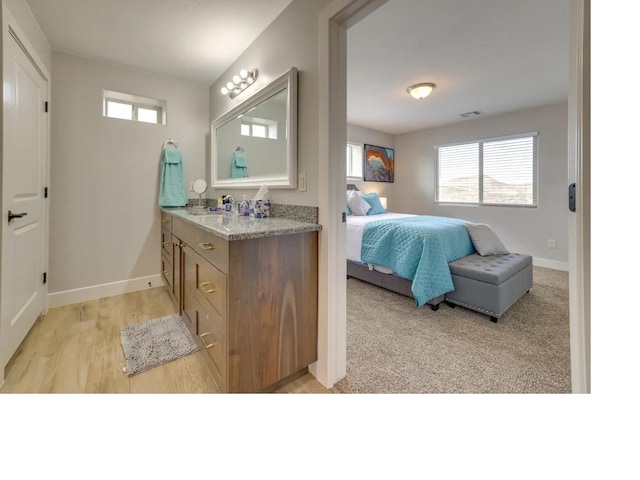 ensuite bathroom featuring a healthy amount of sunlight, vanity, baseboards, and wood finished floors