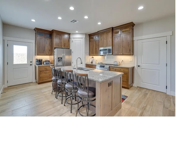 kitchen with a sink, a kitchen breakfast bar, appliances with stainless steel finishes, light wood-type flooring, and tasteful backsplash