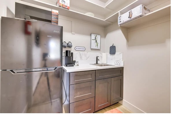 kitchen with light wood finished floors, light countertops, freestanding refrigerator, a sink, and baseboards
