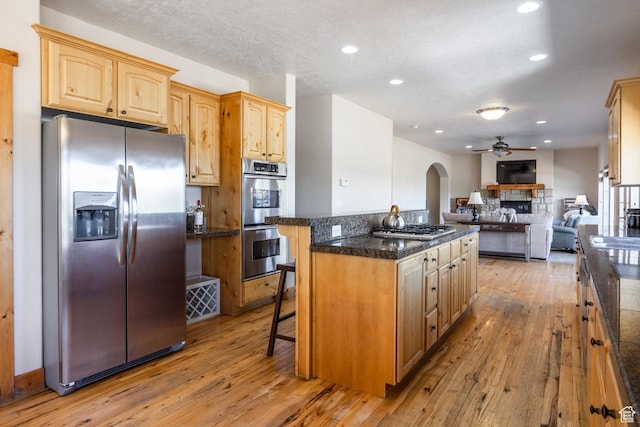 kitchen featuring a center island, open floor plan, arched walkways, stainless steel appliances, and a ceiling fan