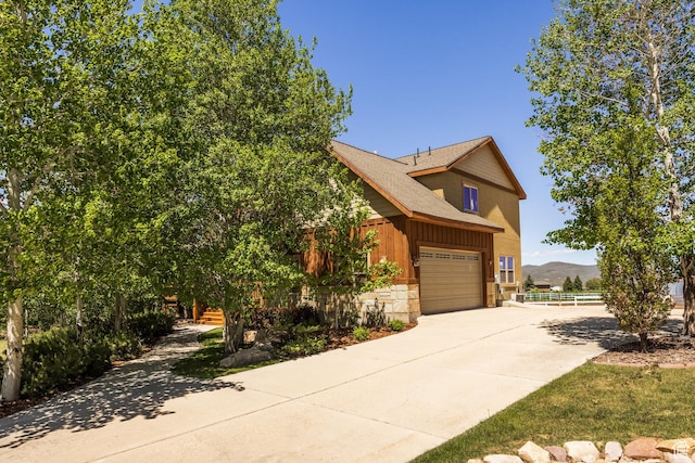 view of front of property with an attached garage, a shingled roof, driveway, stone siding, and a mountain view