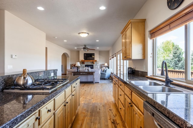 kitchen with a sink, tile countertops, stainless steel appliances, arched walkways, and ceiling fan
