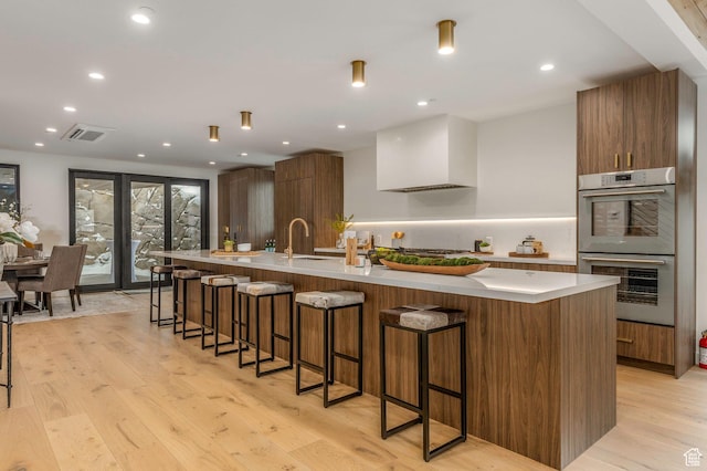 kitchen with modern cabinets, stainless steel double oven, visible vents, a sink, and light wood finished floors