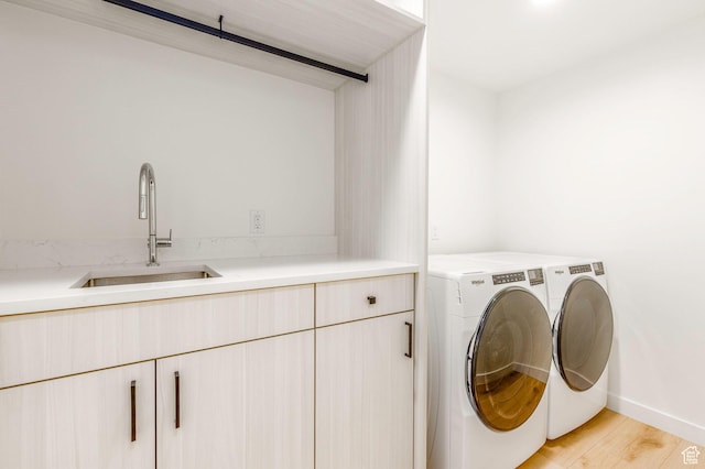 washroom with a sink, washer and clothes dryer, cabinet space, and light wood-style floors
