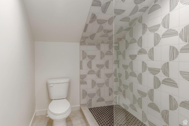 full bathroom featuring toilet, tiled shower, and baseboards