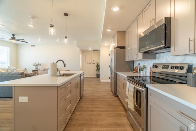 kitchen with appliances with stainless steel finishes, a kitchen island with sink, sink, pendant lighting, and white cabinetry
