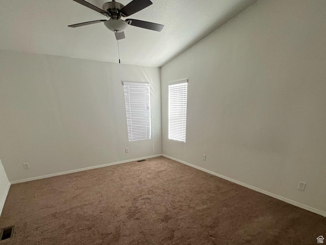 carpeted empty room with lofted ceiling, visible vents, baseboards, and ceiling fan