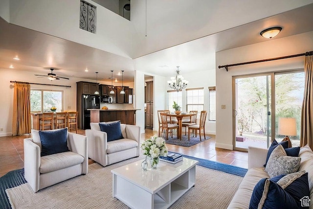 tiled living room featuring ceiling fan with notable chandelier and a high ceiling