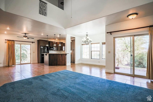 unfurnished living room featuring ceiling fan with notable chandelier, a healthy amount of sunlight, and light tile patterned floors