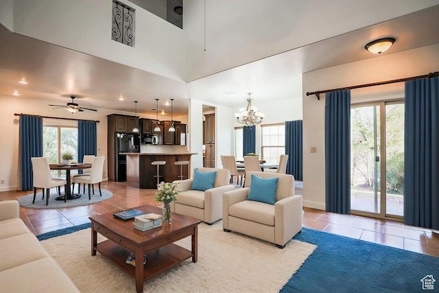 living room featuring a high ceiling, light tile patterned flooring, a healthy amount of sunlight, and ceiling fan with notable chandelier