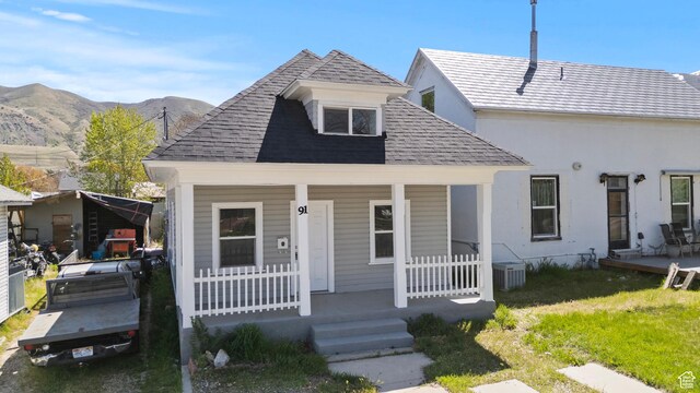 bungalow-style home featuring central AC unit, a front lawn, a shingled roof, a mountain view, and a porch