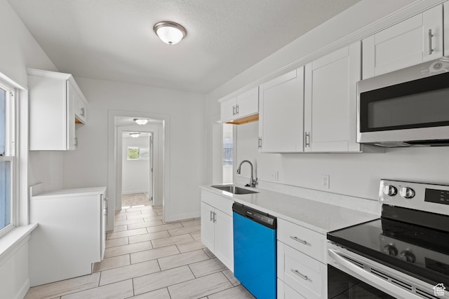 kitchen with a sink, stainless steel appliances, light countertops, white cabinets, and baseboards