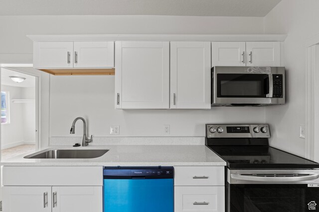 kitchen featuring appliances with stainless steel finishes, light stone countertops, a sink, and white cabinetry