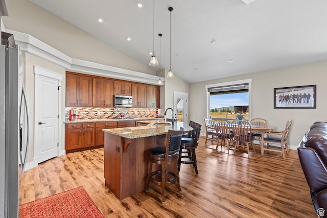 84 W 2100 N, Kamas, UT 84036 - kitchen featuring light stone counters, stainless steel appliances, light wood-style flooring, brown cabinetry, and a kitchen breakfast bar