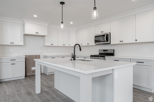 kitchen with white cabinets, hanging light fixtures, an island with sink, light wood-type flooring, and stainless steel appliances