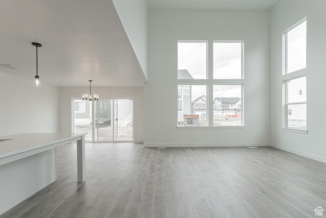 unfurnished living room featuring a wealth of natural light, a high ceiling, wood-type flooring, and an inviting chandelier
