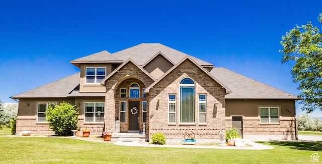 view of front of property with a shingled roof, a front lawn, and brick siding