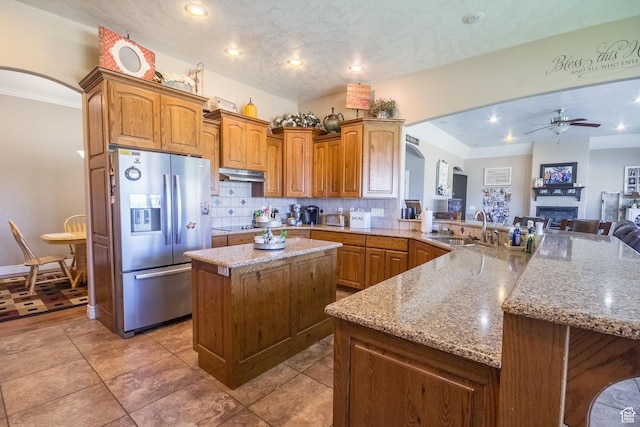 kitchen featuring ceiling fan, arched walkways, stainless steel refrigerator with ice dispenser, under cabinet range hood, and a sink