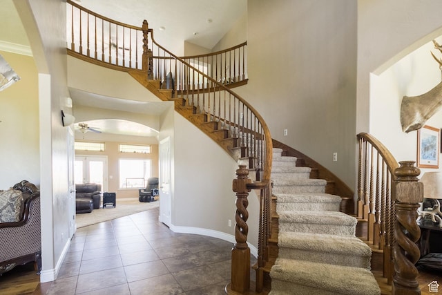 stairs featuring baseboards, arched walkways, a ceiling fan, a towering ceiling, and tile patterned flooring