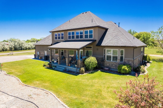 back of house with a yard, a shingled roof, stucco siding, and stone siding