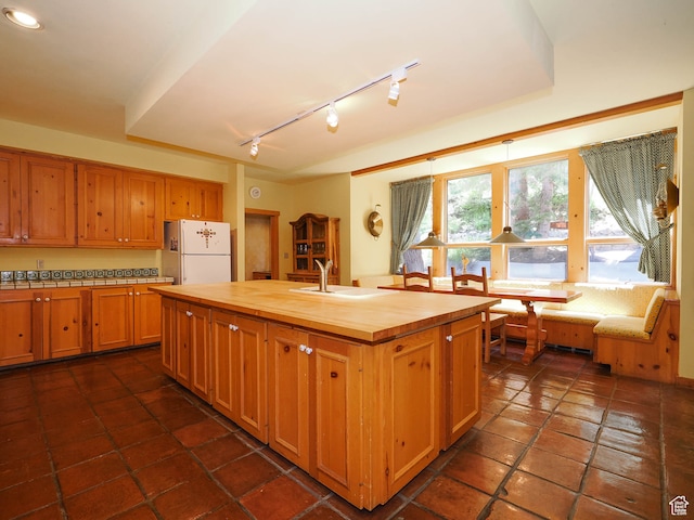 2718 E Stewart Rd, Sundance, UT 84604 - kitchen with white refrigerator, a kitchen island with sink, dark tile flooring, wooden counters, and sink
