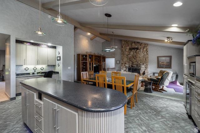kitchen with dark countertops, a stone fireplace, beam ceiling, and open floor plan
