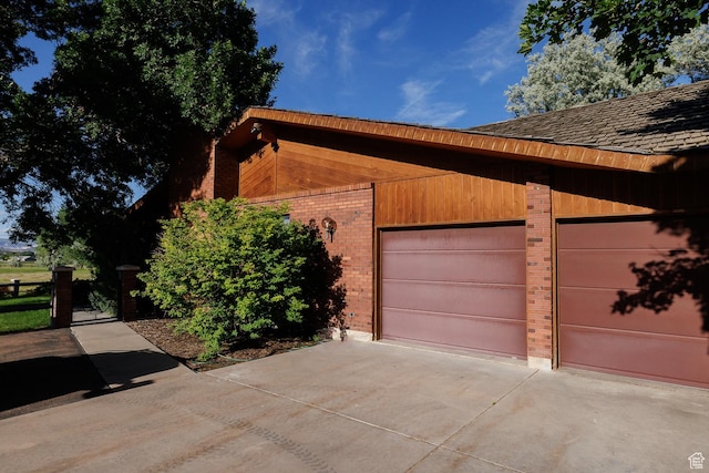 view of home's exterior featuring concrete driveway, an attached garage, brick siding, and a gate