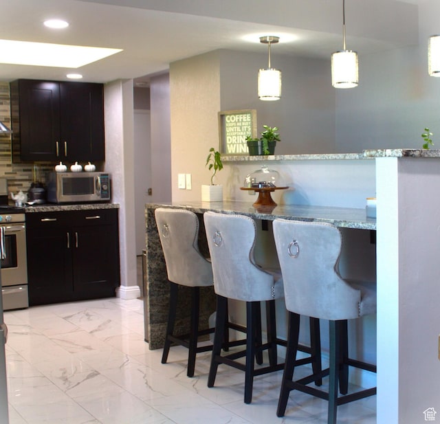 7642 S 2700 W, West Jordan, UT 84084 - kitchen with appliances with stainless steel finishes, a kitchen breakfast bar, light stone counters, dark brown cabinets, and pendant lighting