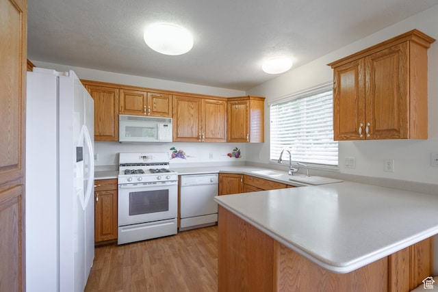 kitchen with white appliances, sink, light wood-type flooring, kitchen peninsula, and a breakfast bar area
