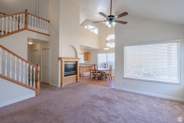 unfurnished living room featuring ceiling fan, a towering ceiling, and light colored carpet