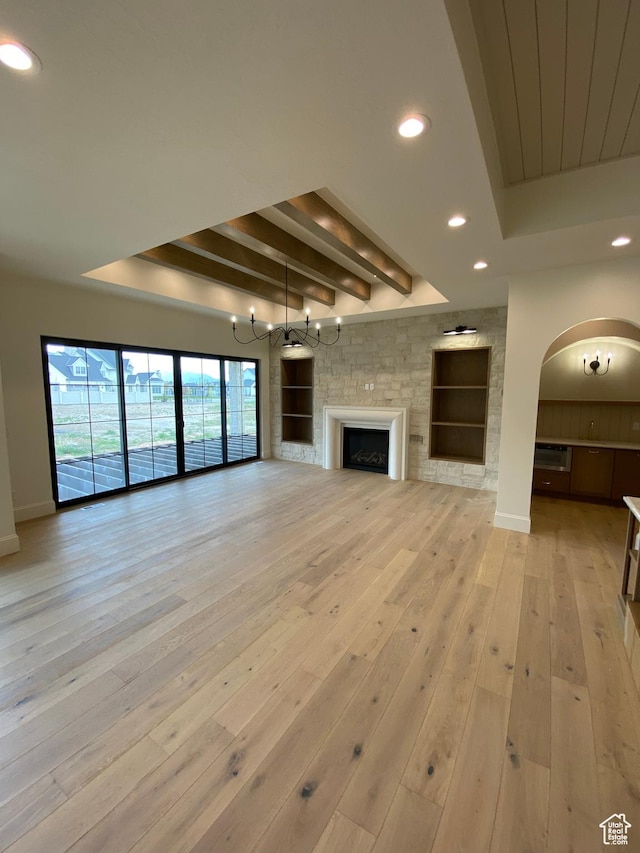 unfurnished living room with recessed lighting, arched walkways, a tray ceiling, and light wood-style flooring