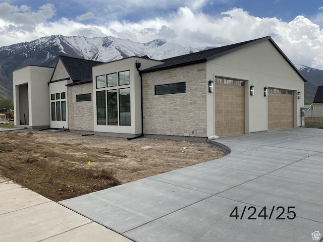view of home's exterior featuring concrete driveway, stone siding, an attached garage, a mountain view, and stucco siding