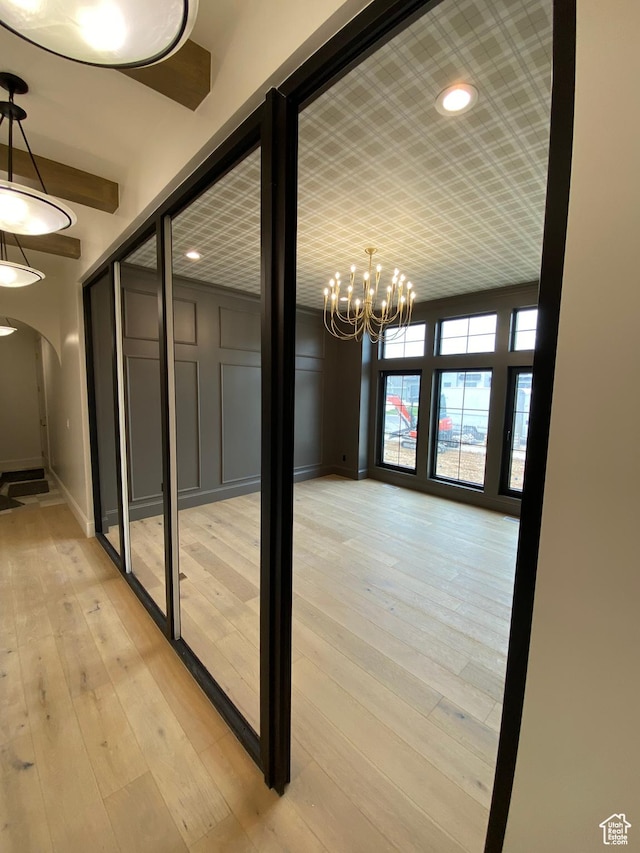 hallway with arched walkways, light wood-type flooring, baseboards, and a notable chandelier