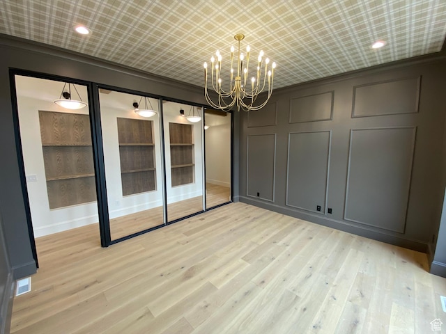 unfurnished room featuring baseboards, an inviting chandelier, light wood-style floors, and a decorative wall