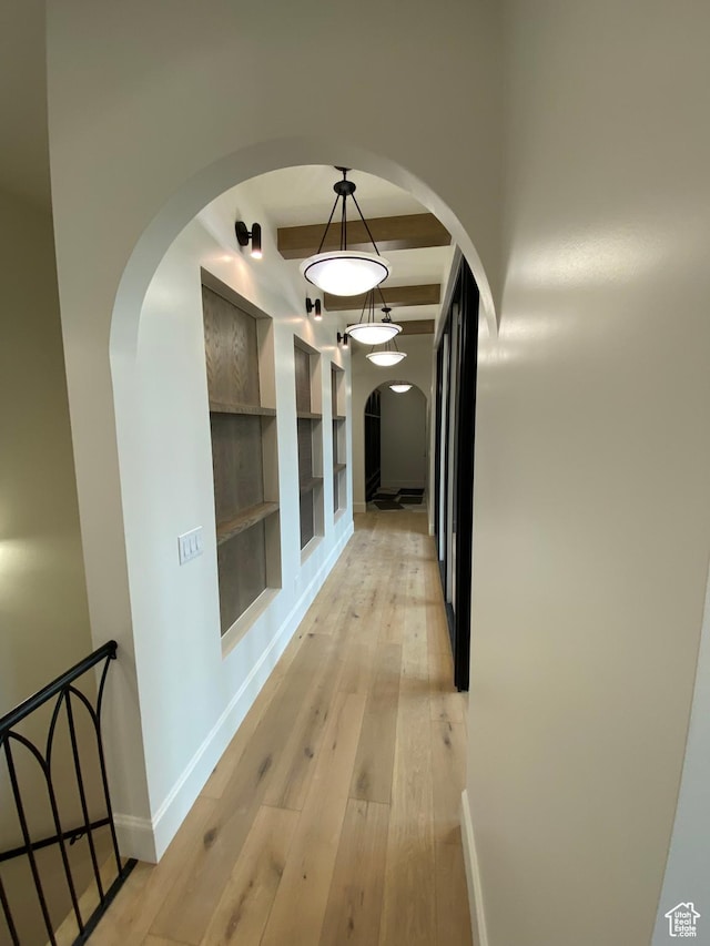 hall featuring arched walkways, beamed ceiling, baseboards, light wood-style flooring, and built in shelves