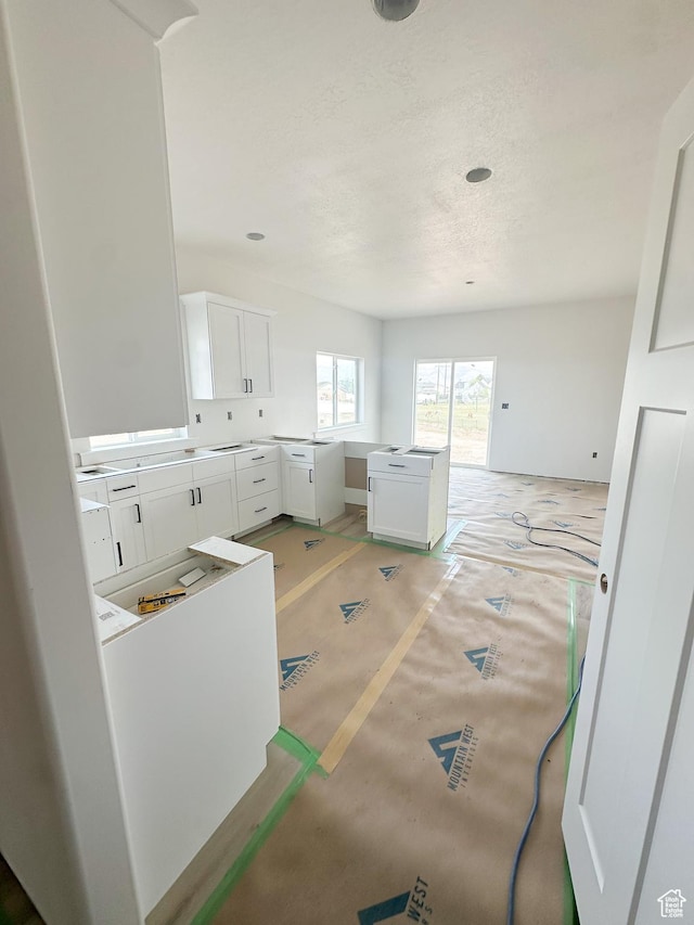 kitchen with light colored carpet, white cabinets, baseboards, and a textured ceiling