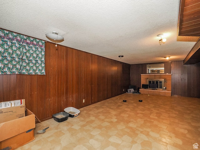 basement with a brick fireplace, wooden walls, a textured ceiling, and light tile floors