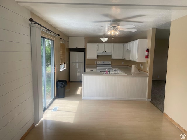 kitchen with light countertops, a peninsula, under cabinet range hood, white appliances, and visible vents