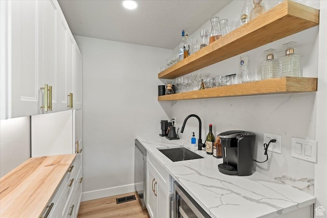 bar with dishwasher, sink, white cabinets, light stone counters, and light wood-type flooring