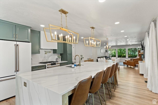 kitchen featuring pendant lighting, sink, light stone counters, premium appliances, and green cabinetry