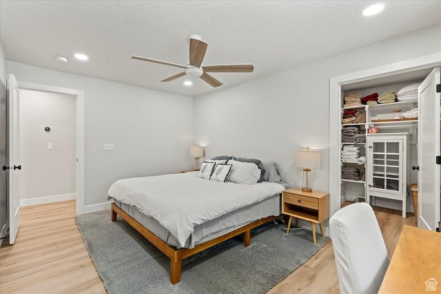 bedroom featuring ceiling fan, a textured ceiling, a spacious closet, a closet, and light wood-type flooring