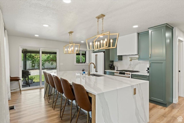 kitchen featuring high quality appliances, light stone countertops, green cabinets, and hanging light fixtures