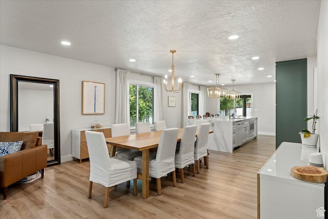 dining area with a healthy amount of sunlight, a textured ceiling, light hardwood / wood-style flooring, and a notable chandelier