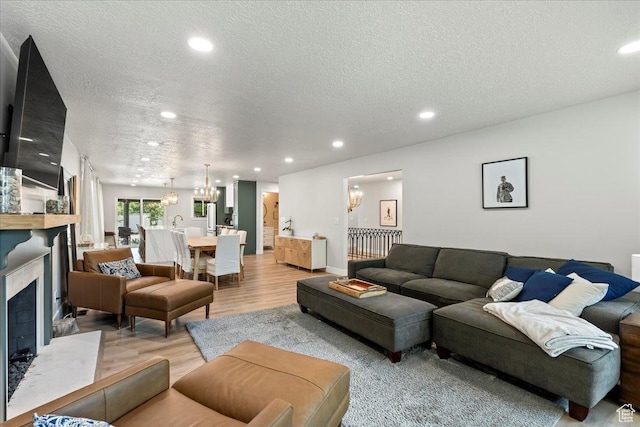 living room featuring a notable chandelier, a high end fireplace, a textured ceiling, and light wood-type flooring