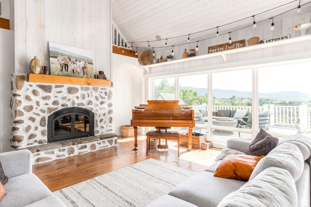 living room with vaulted ceiling, track lighting, a stone fireplace, wood-type flooring, and a mountain view