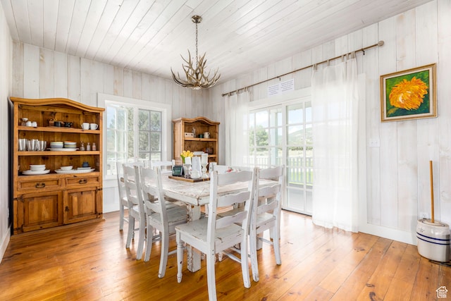 dining room with wooden walls, light hardwood / wood-style flooring, a notable chandelier, and wood ceiling
