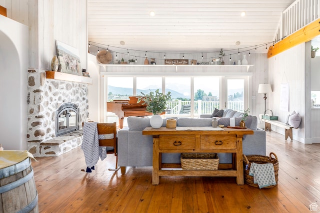 living room featuring a high ceiling, a stone fireplace, rail lighting, and wood-type flooring