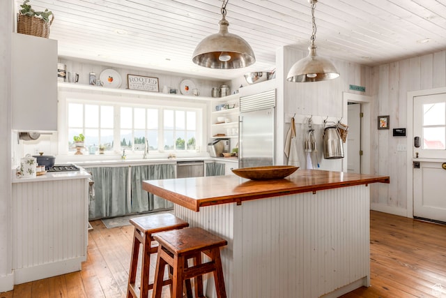 kitchen with light hardwood / wood-style floors, wood counters, a kitchen island, appliances with stainless steel finishes, and pendant lighting