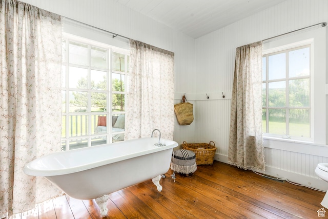 bathroom with a bath, toilet, and hardwood / wood-style flooring