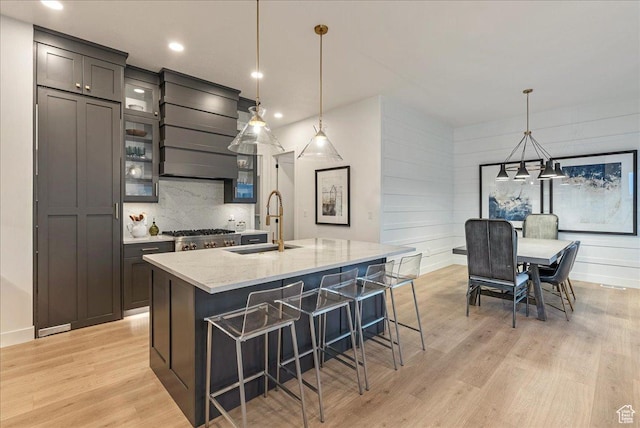 1901 S Sawmill Blvd E Unit 415, Heber City, UT 84032 - kitchen featuring light wood-type flooring, light stone counters, sink, a center island with sink, and hanging light fixtures